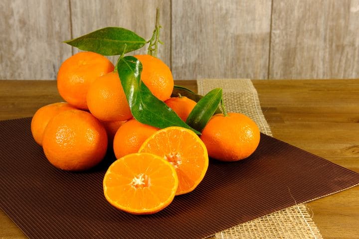 A wooden table with mandarin oranges arranged on top, some of them sliced in half, with a napkin placed underneath