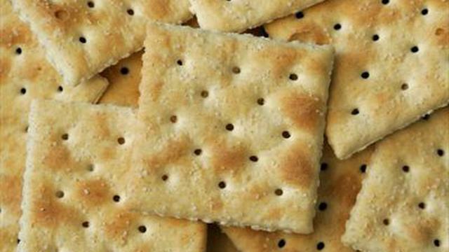 An open arrangement of 5 to 7 saltine crackers scattered loosely, with visible grains of salt on their surfaces.