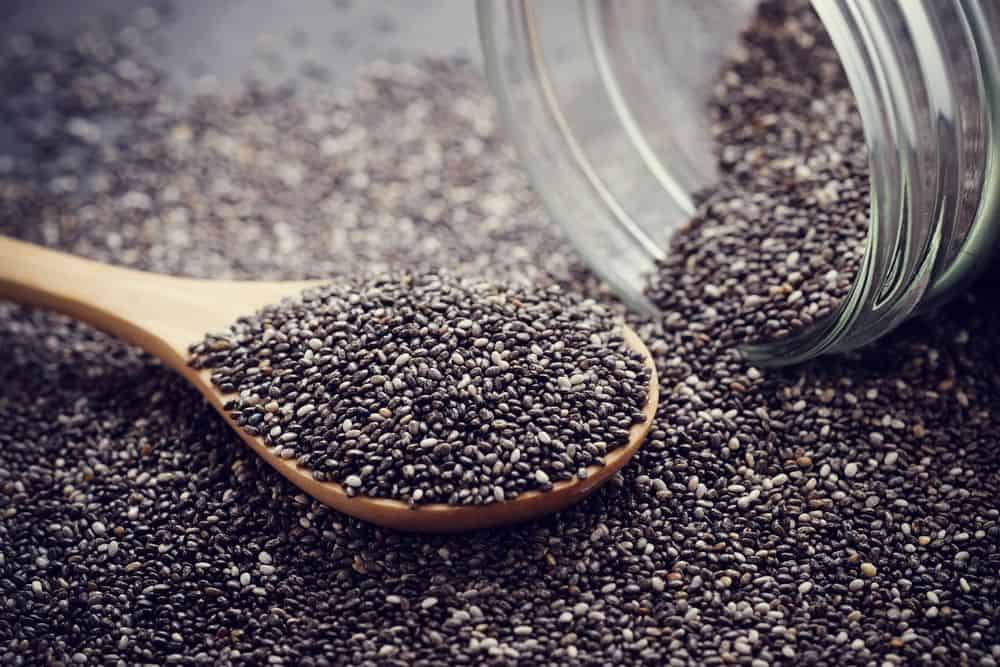 wooden spoon filled with black and white chia seeds spilling out of a glass jar