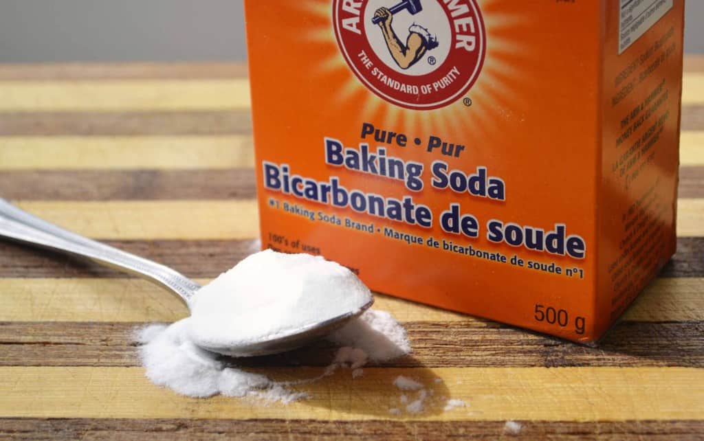 Box of baking soda with a spoonful spilling onto a wooden surface.
